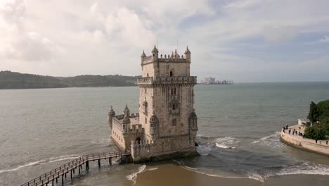 slow rising shot of the torre de belém with waves crashing onto the beach