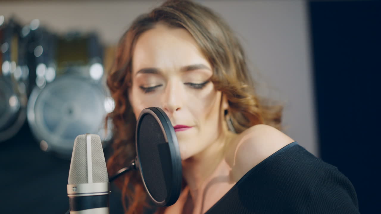 beautiful singer with curly hair is singing a song in an audio recording studio on the background of professional equipment. Close-up