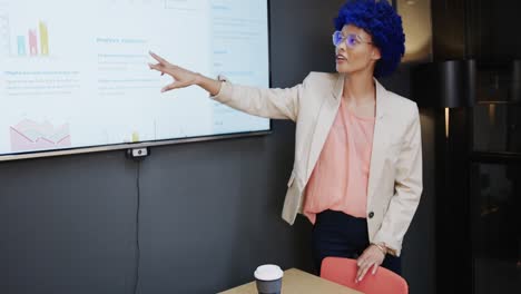 biracial casual businesswoman with blue afro making presentation in office, slow motion