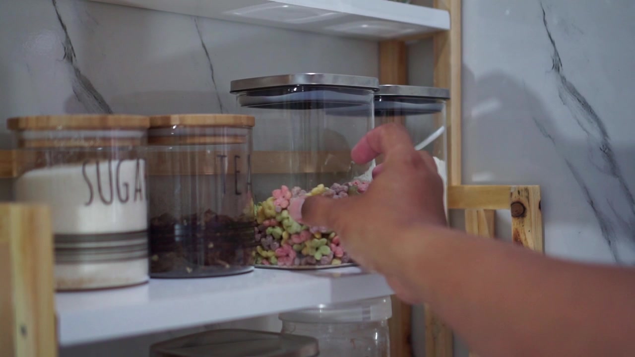 Mano che ripone un contenitore colorato di cereali sullo scaffale, concetto di organizzazione della dispensa e della casa.