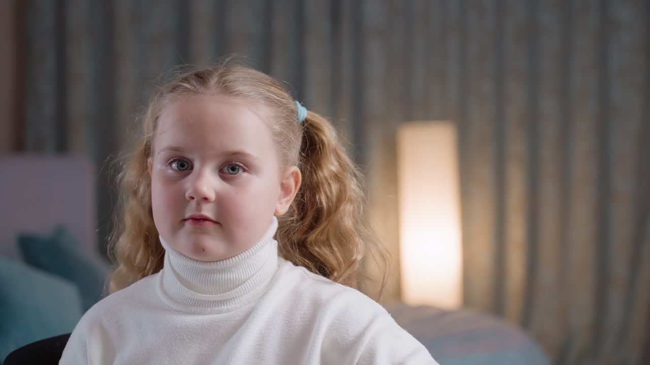 Young girl with blonde hair in ponytails wearing white turtleneck holding up drawing on paper close to face, eyes peeking over artwork, showing innocent pride, creativity, childhood expression