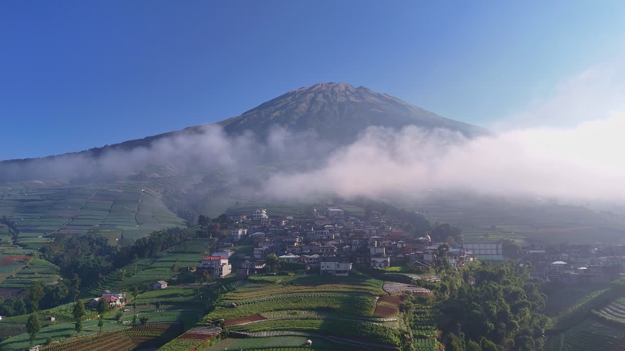 Splendido paesaggio di un insediamento rurale sul pendio di una montagna, con nebbia mattutina e cielo azzurro terso. Monte Sumbing, Indonesia