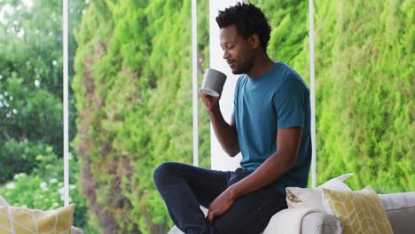 Relaxed-biracial-man-sitting-on-patio-and-drinking-coffee