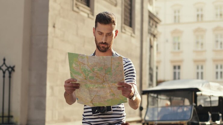 Lost Male Tourist Holding A City Map And Looking For Directions In The Old Town Street