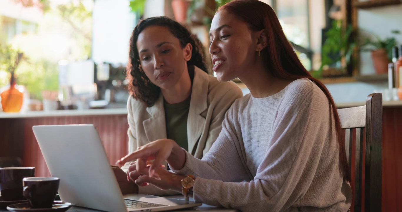 Two Professional Women Collaborating on a Laptop in a Cafe