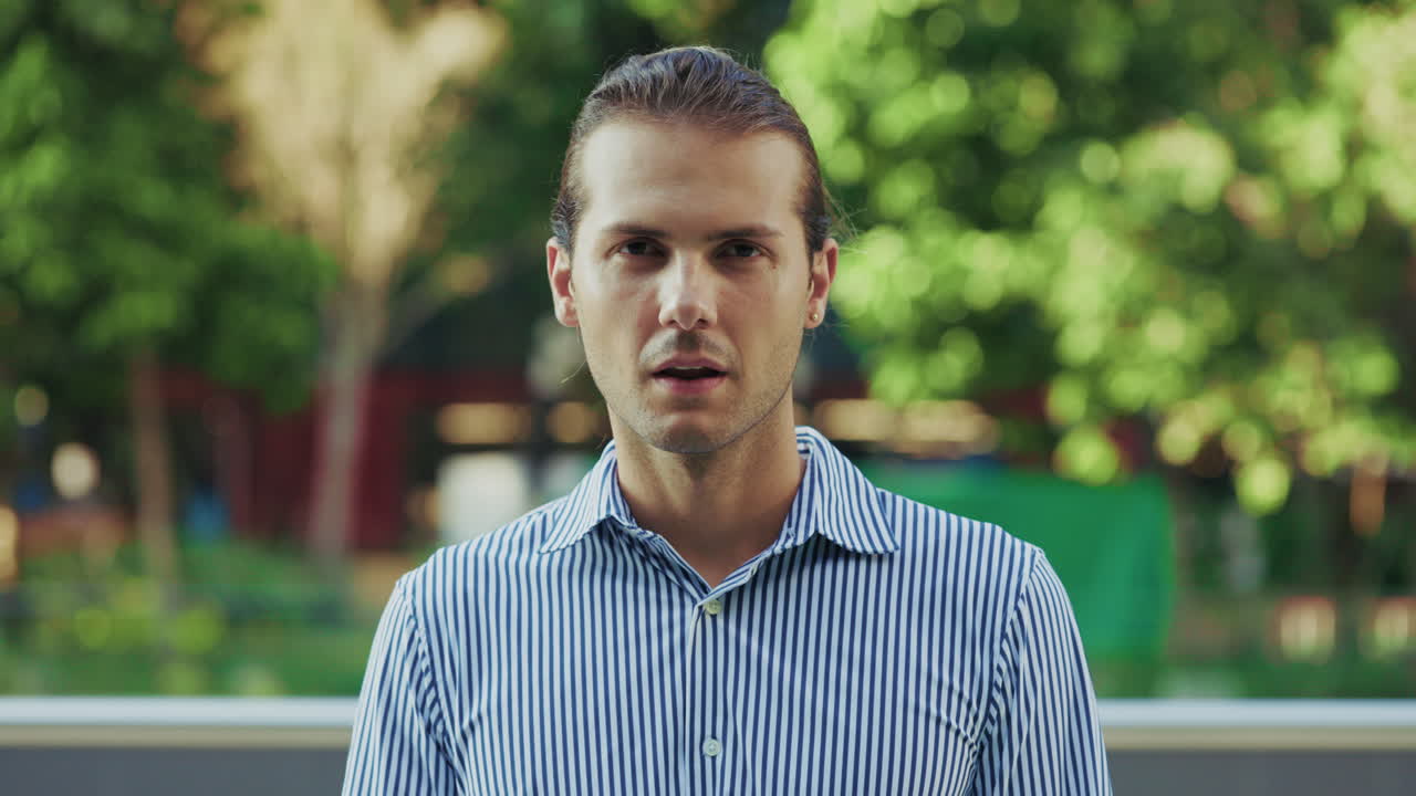 Young Man in Striped Shirt Making a Hand Gesture Outdoors