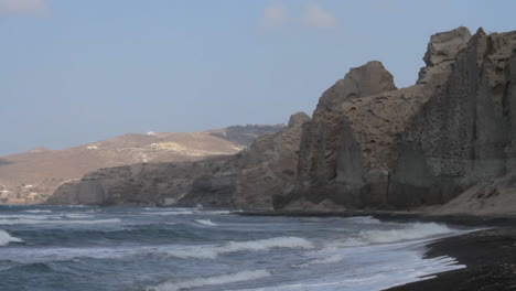 Time-Lapse-of-a-black-sand-beach-surrounded-by-white-volcanic-cliff-formations-in-Santorini,-Greece