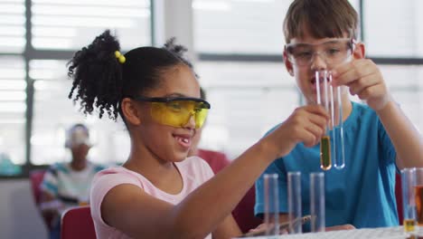 escolares de diversas razas con gafas de protección sosteniendo tubos de ensayo durante la clase de química