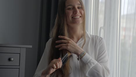 sonriente joven morena feliz cepillándose el cabello, vista frontal