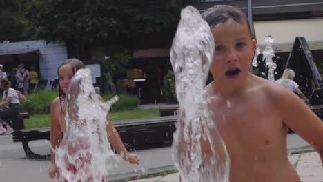 Slow-motion-shot-of-a-boy-in-a-swimsuit-running-through-a-stream-of-water-in-a-city-fountain