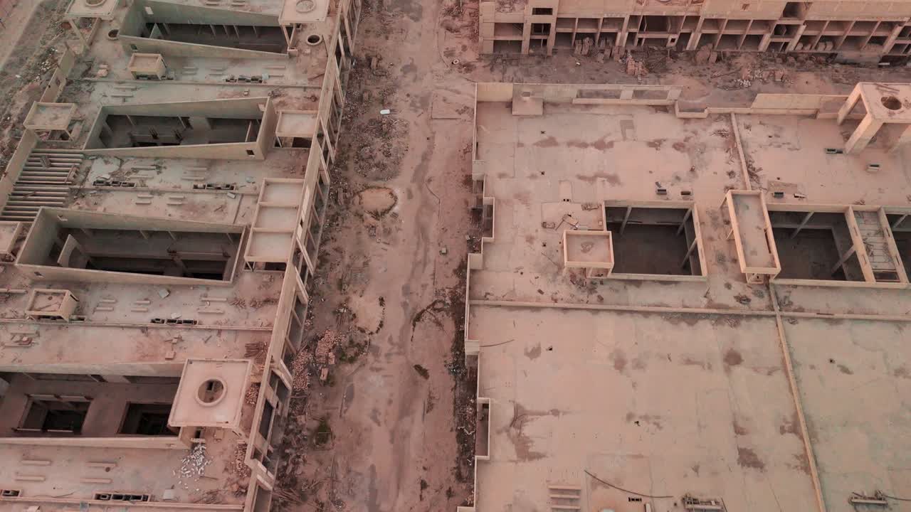 Ripresa aerea dall’alto di un incrocio abbandonato all'interno di un complesso di cemento incompiuto, con cumuli di macerie, colonne a vista, materiali sparsi e strade di accesso vuote: concetto di degrado urbano e ispezione