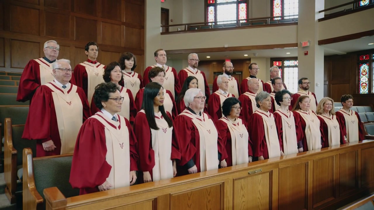 Clapping choir members lowering hands after conductor cue in sanctuary, wearing maroon cream robes