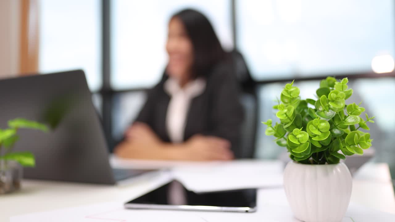 Professionelle Frau mit Laptop in hellem Büro, Fokus wechselt zwischen ihr und der Büropflanze