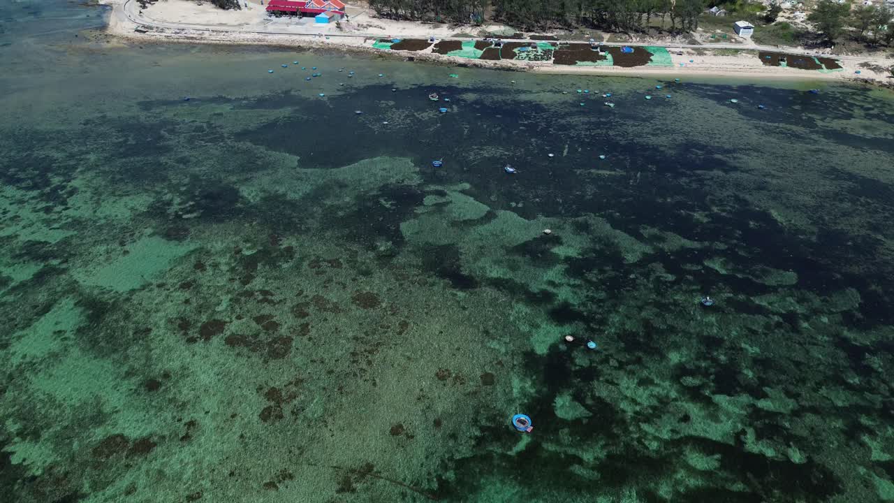 A forward and upward aerial shot revealing fishing boats anchored near the coastline and a small fishing village in Ninh Hải, Vietnam.