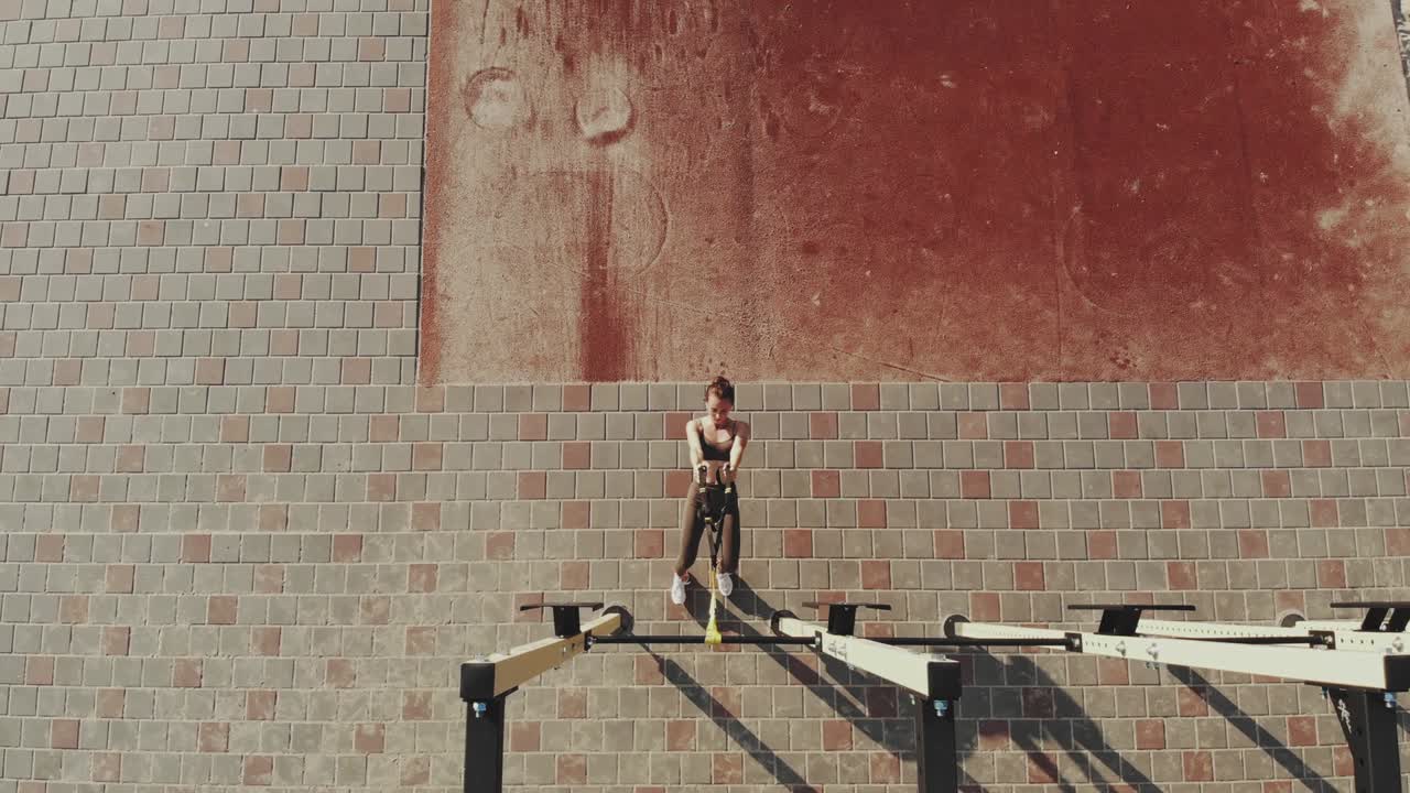 entrenamiento al aire libre. correas de suspensión. aero vista superior. mujer joven atlética está haciendo ejercicios de resistencia de todo el cuerpo usando cuerdas en bucle trx, en el campo deportivo al aire libre de la ciudad, gimnasio. entrenamiento de fitness al aire abierto. concepto de estilo de vida saludable. entrenamiento deportivo matutino en el
