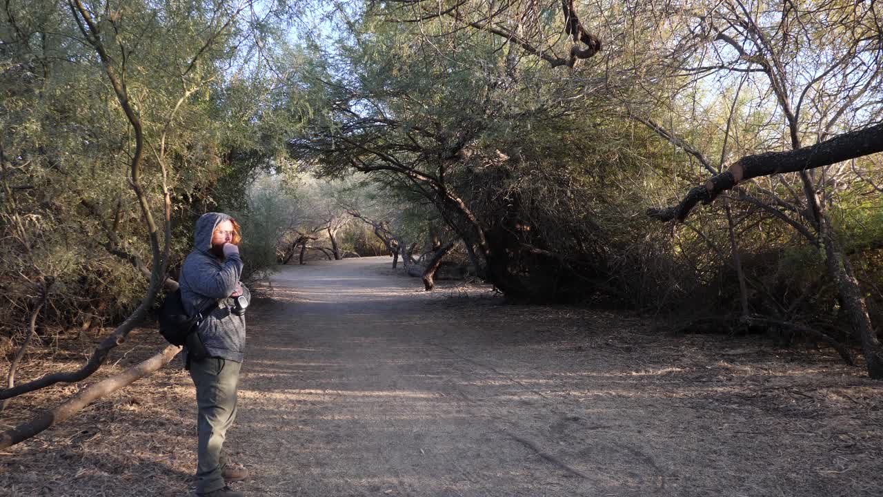 un hombre pelirrojo camina y vapea en un parque.