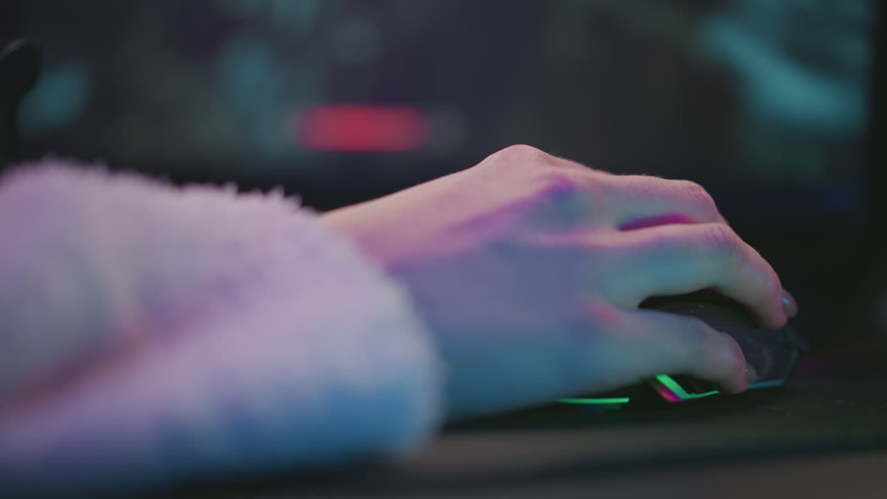 closeup hand of female gamer using gaming mouse during video game session, colorful ambient light reflecting on skin and sleeve while screen displays gameplay in background with soft focus