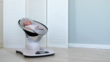 sweet newborn baby girl sleeping in a bouncer chair in a white room