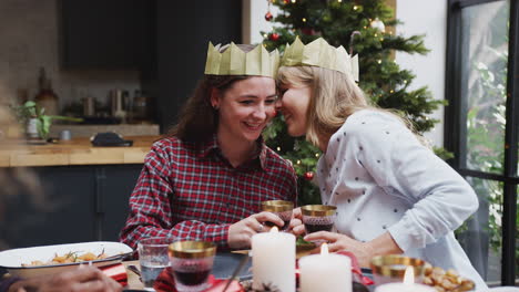 pareja gay sentada alrededor de la mesa para la cena de navidad susurrando y haciendo un brindis