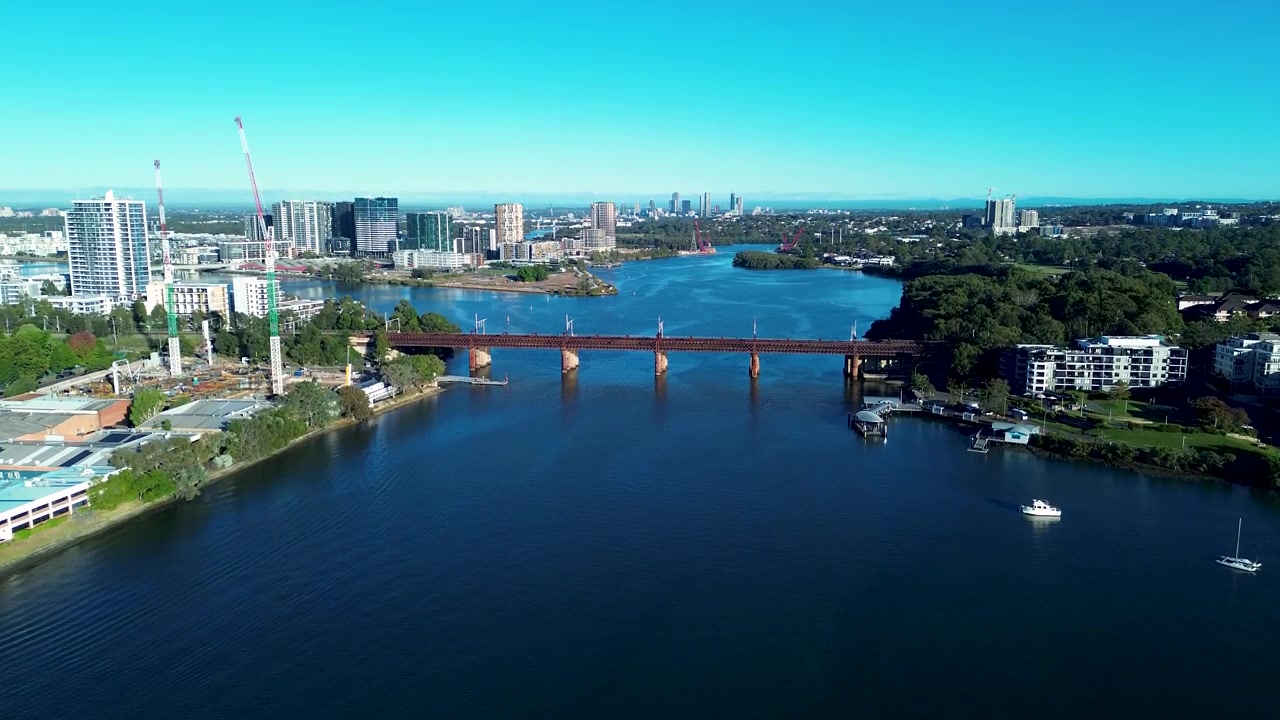 Drone-ilmakuva Parramatta-joen rautatiesillasta, jota ympäröivät kaupunkirakennukset ja rakennusnosturit ranta-alueen laiturilla lähellä Meadowbankia Sydneyn kaupungissa Australiassa. Infrastruktuuri.