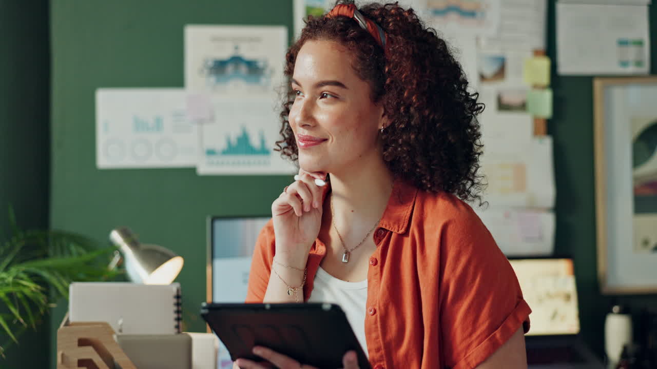 A woman with curly hair is using a tablet in her office