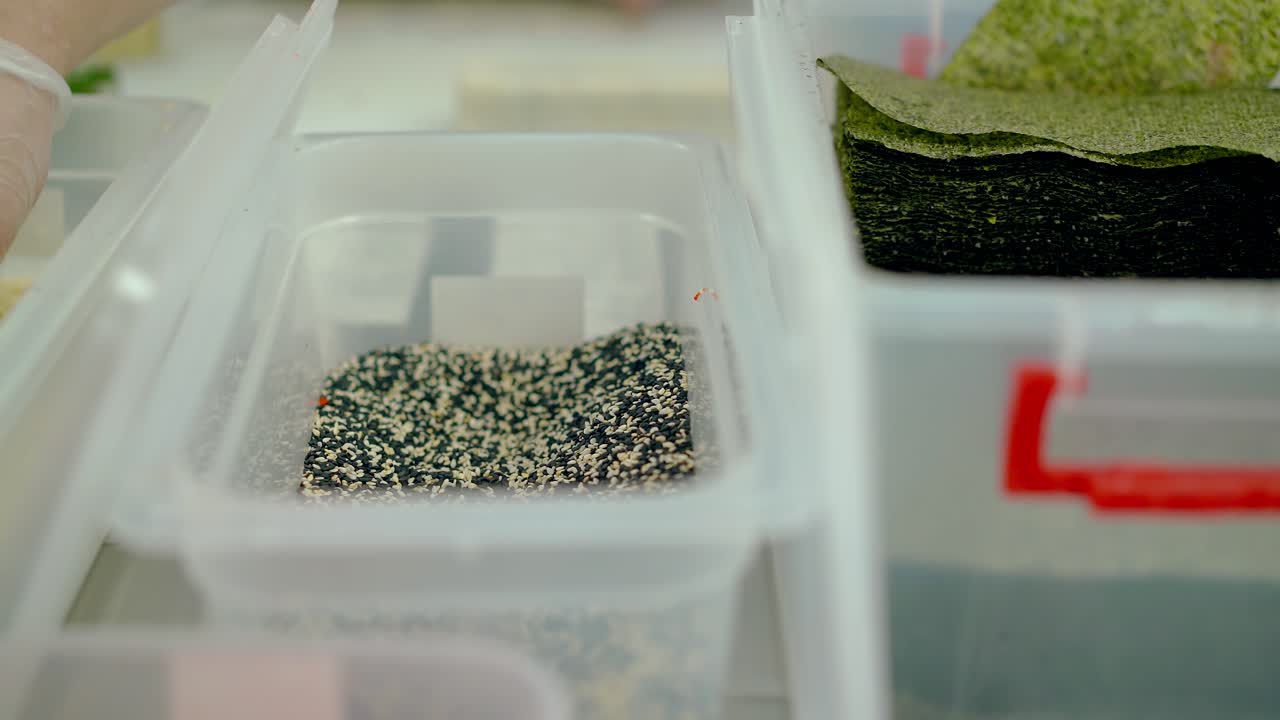 요리사는 세사미 용기에서 일본 롤을 위한 공작품을 꺼 ⁇ 니다.