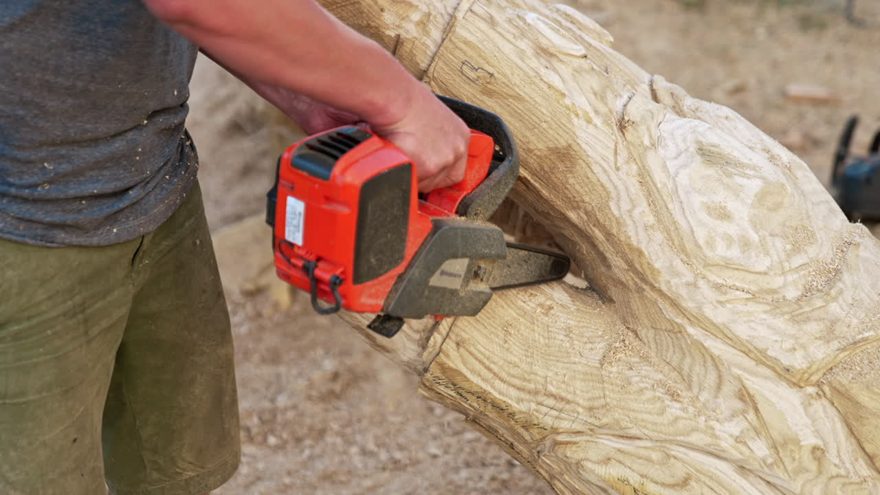 Unrecognized hands of a male artist working with a chain saw. Man making a wooden sculpture of a hand.