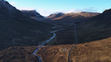 glencoe valley with winding river and road amidst rugged mountains, daylight, aerial view