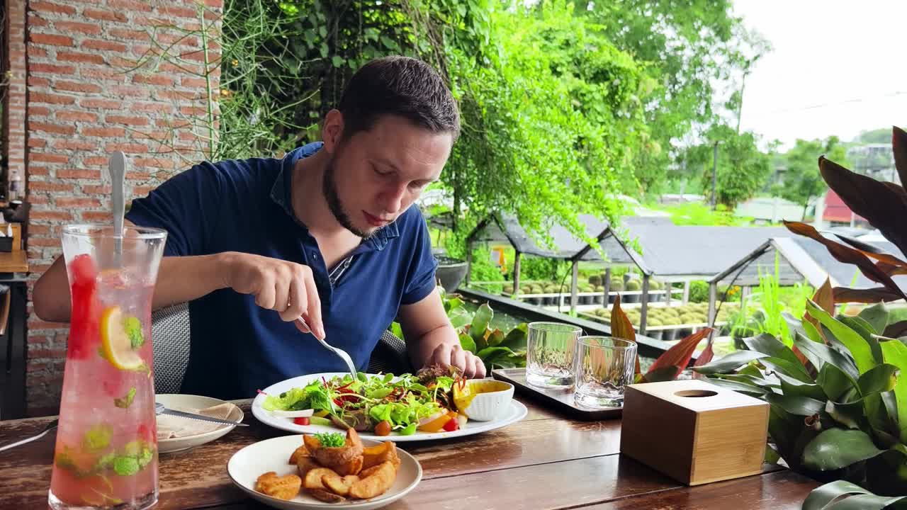 hombre comiendo ensalada de carne en una cafetería al aire libre
