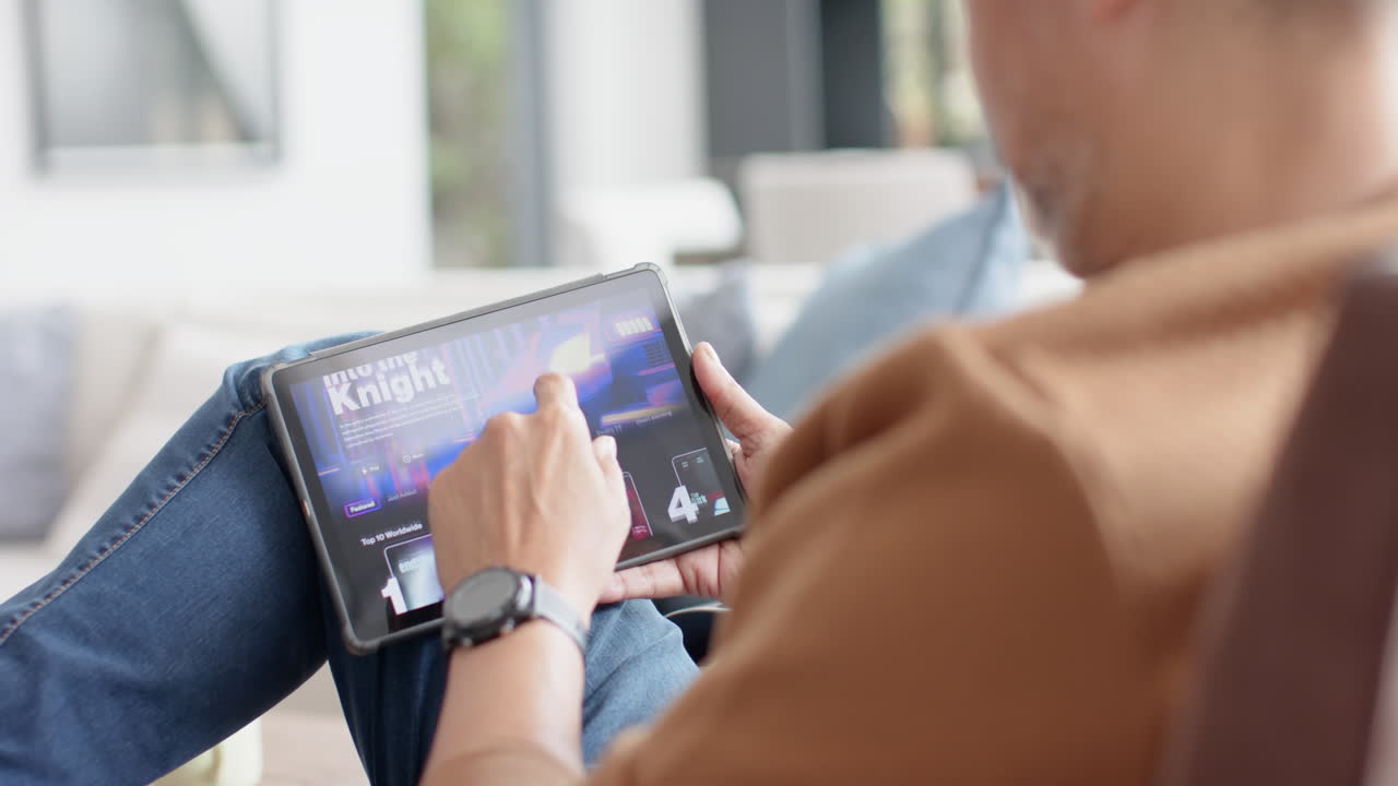 Senior biracial man using tablet sitting in sunny living room at home, slow motion