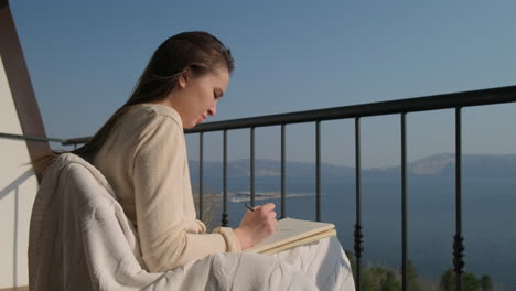 woman writing on a balcony with a view of the lake and mountains