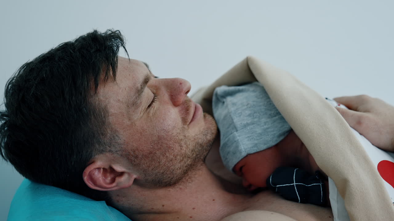Caucasian dad is happy to hold his just born child. The baby is put on father's chest for skin to skin contact.