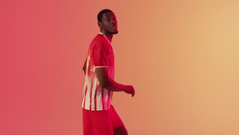 African-american-male-soccer-player-returning-football-over-neon-pink-lighting