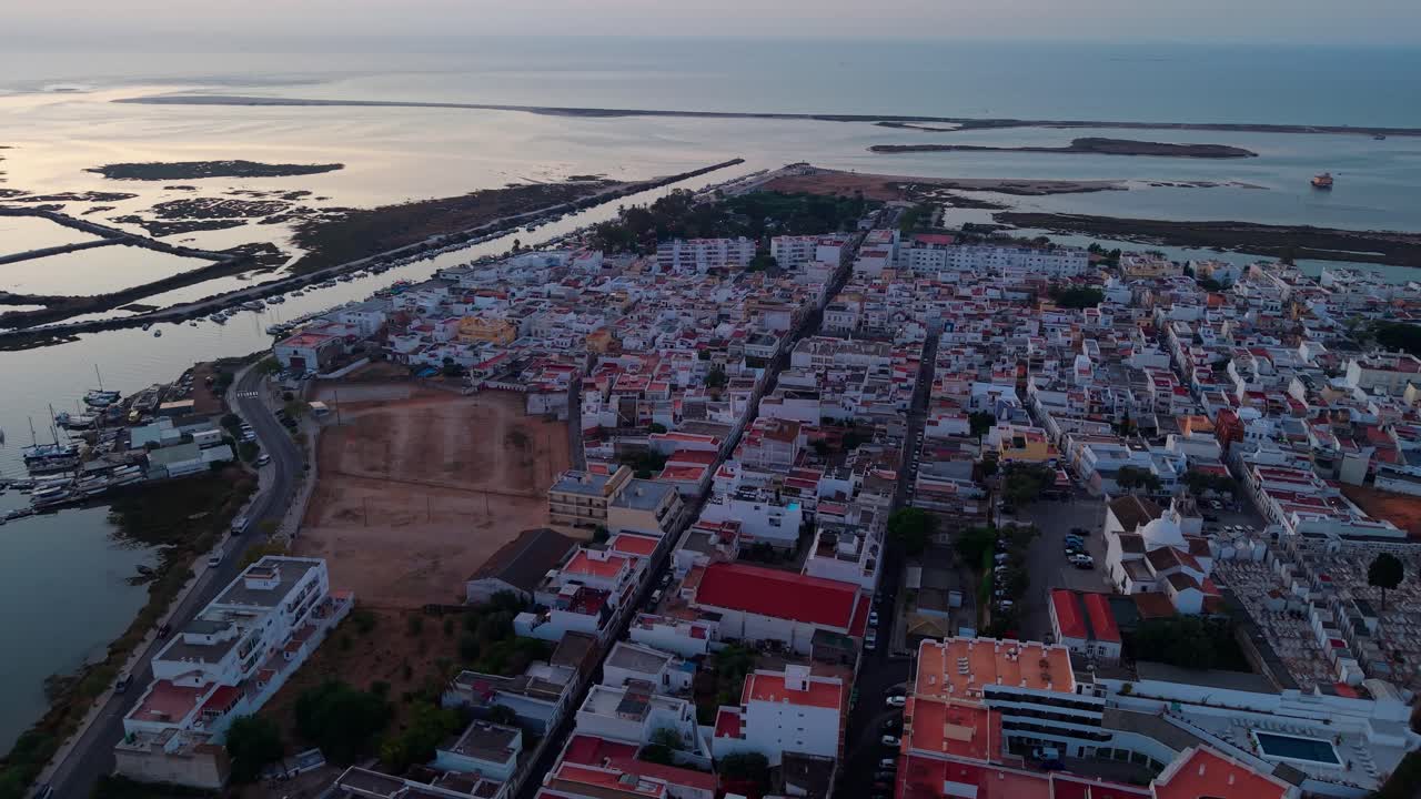 aerial shot over Fuseta, typical fishing village in Algarve region near Ria formosa natural park and Faro at sunrise with the village in the foreground and the salt pans in the background. Portugal