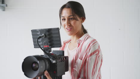 Female-Videographer-With-Video-Camera-Filming-Movie-In-White-Studio