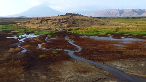 an incredible drone shot of the stunning landscape of lake natron with people standing on a hill top with ol doinyo lengai volcano in the background in tanzania in north africa