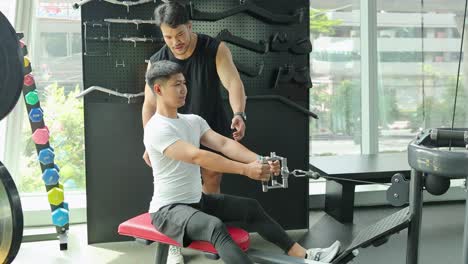 a man exercises on a cable machine with guidance from a trainer in a well-lit gym
