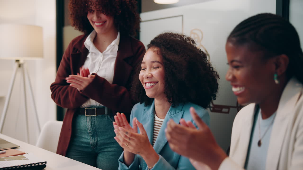Three women clapping and smiling in a business meeting