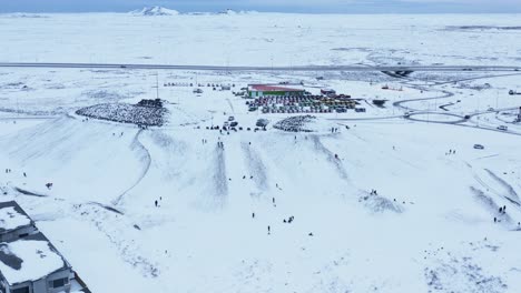 local iceland people enjoying white snow winter fun sliding down hill on sleds, aerial