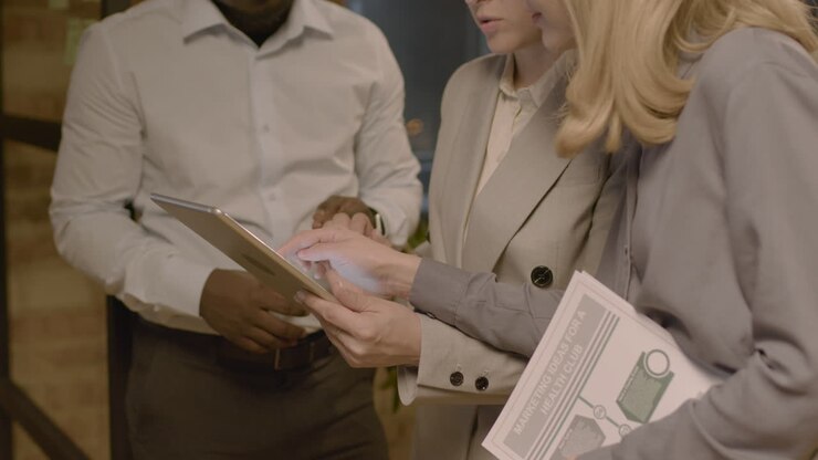 Gruppo di tre impiegati in piedi in ufficio, che analizzano dati su un tablet e discutono insieme la strategia di marketing 2