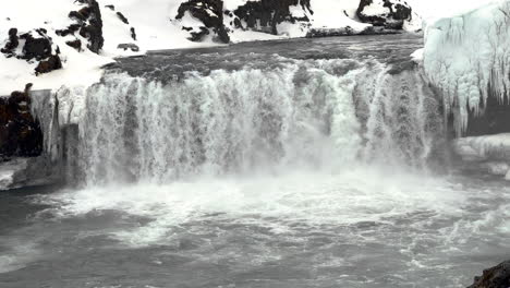 slow motion shot of deluge of water crashing down icy waterfall in winter - goðafoss,iceland