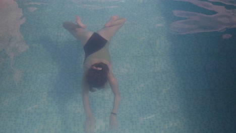 a young woman swims underwater toward the camera in a swimming pool