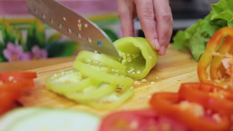 manos femeninas de la ama de casa con un cuchillo cortado pimienta fresca en la mesa de la cocina de la mesa de corte