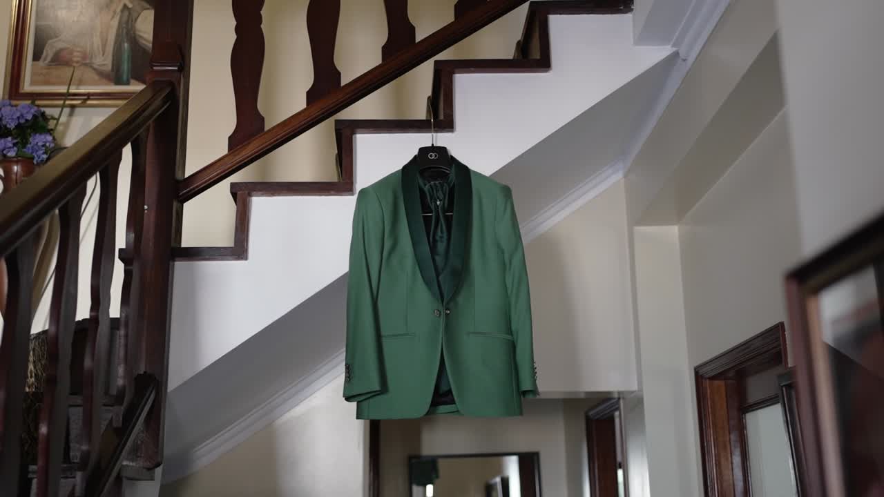 Green groom suit on a hanger suspended in a vintage home staircase setting