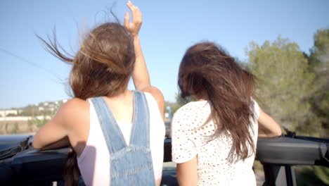 two female friends standing up in the back of a moving car