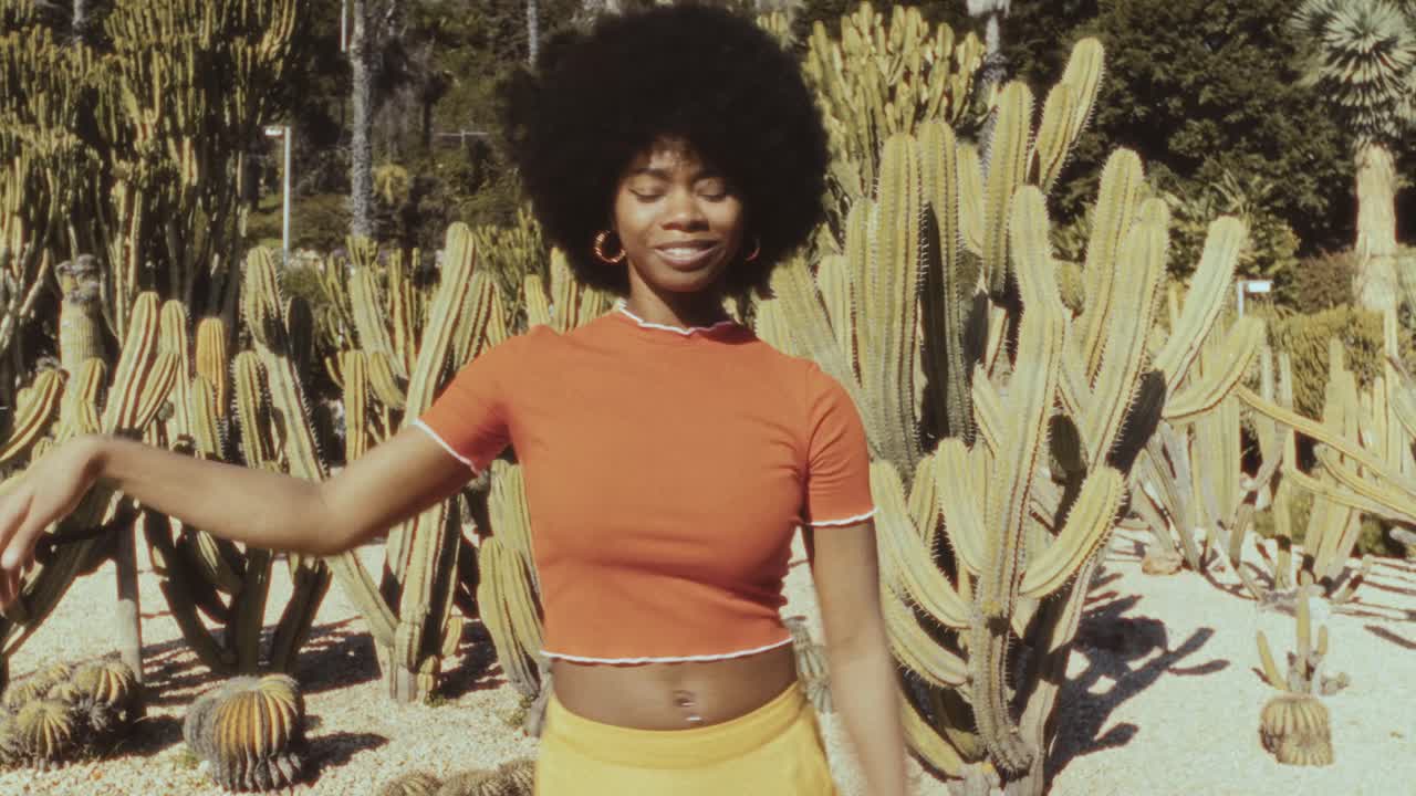Giovane donna di colore con afro che balla felicemente in un giardino di cactus