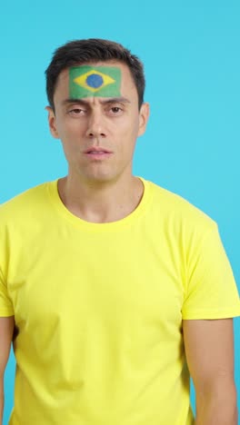 man standing with brazilian flag painted on face smiling