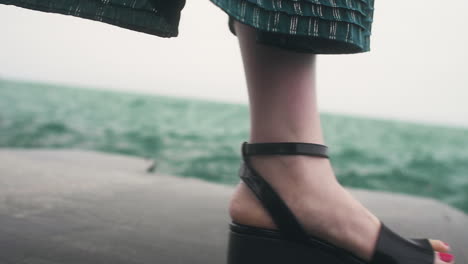 water splashes against the feet of a japanese woman as she walks in her tall black shoes along the lake