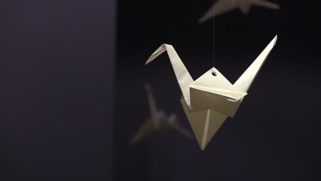 grulla de origami de papel blanco colgando en una habitación oscura