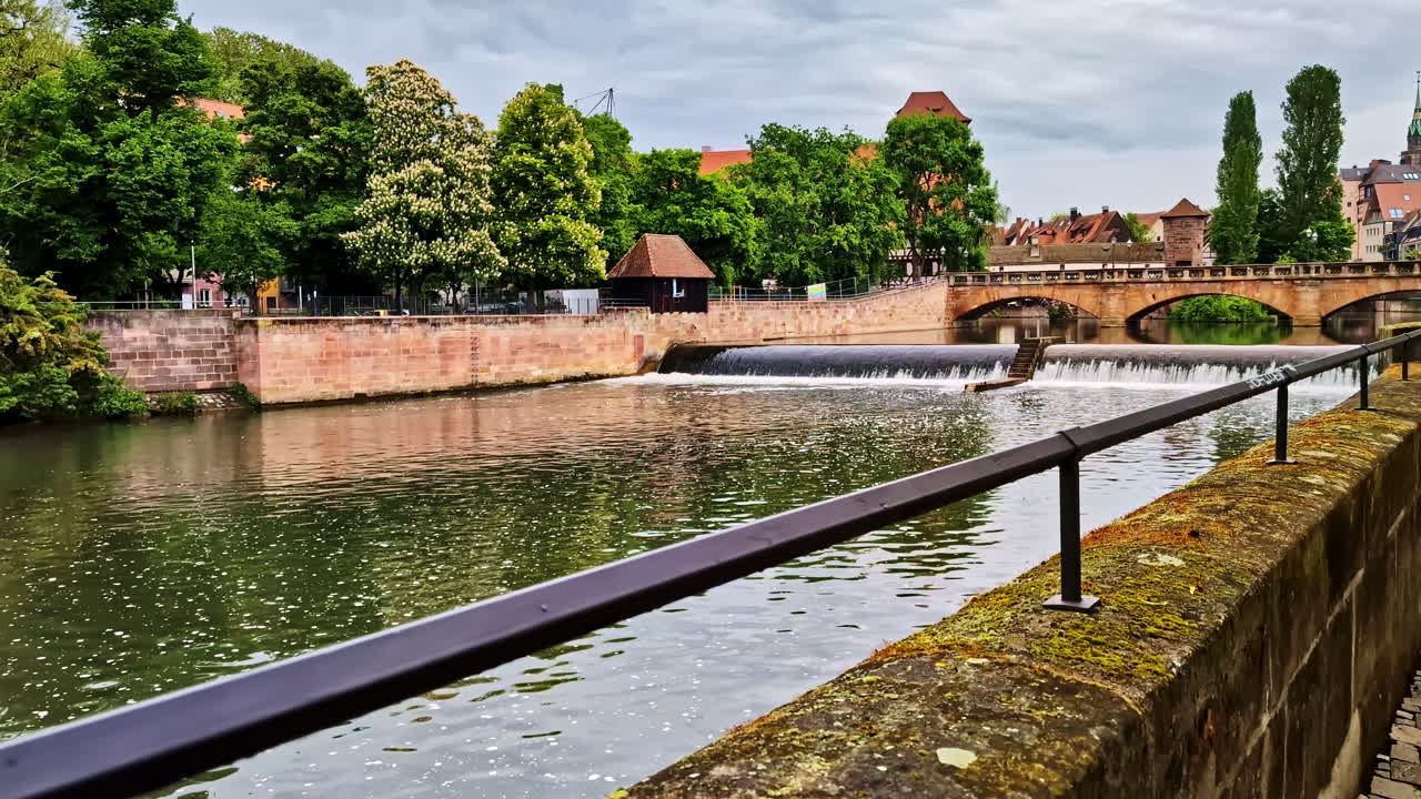 Maxbrucke bridge spans the Pegnitzwehr weir on the Pegnitz River in Nuremberg, Germany, in daylight, water spills over small levee